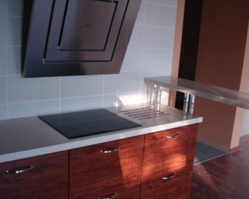 Lesklá kuchyňská linka s černou varnou deskou a skleněným zábradlím