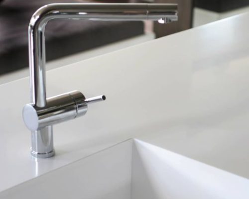 Detail bílé kuchyňské baterie u moderního dřezu