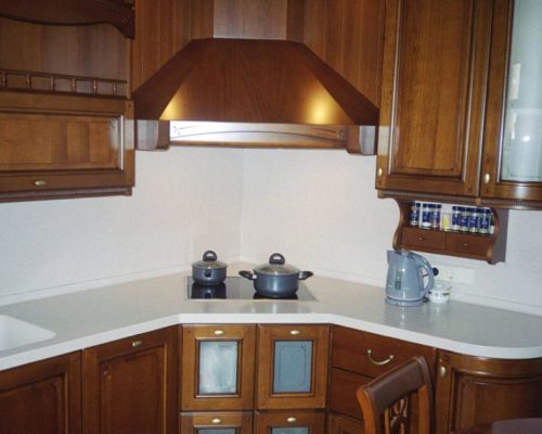 Rohová kuchyň s dřevěnými skříňkami a nerezovou digestoří